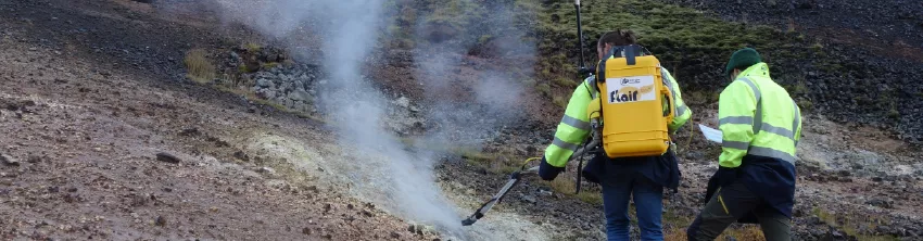 Deux techniciens en gilet fluorescent réalisant des mesures près d'une fumerolle volcanique