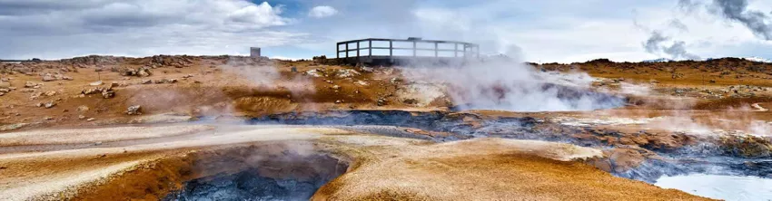 Site géothermal fumant avec bassins de boue et passerelle en bois