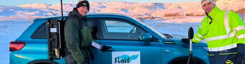 Deux techniciens réalisant des mesures avec un équipement portable à côté d'un véhicule Flair, dans un paysage enneigé