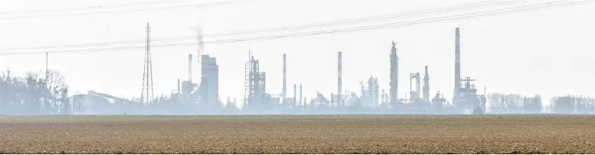 Site industriel aux cheminées fumantes dans la brume, derrière un champ labouré