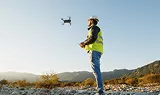 Technicien en casque et gilet de sécurité pilotant un drone sur un terrain rocailleux