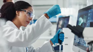 Chercheuse en blouse, gants et lunettes de protection utilisant une pipette dans un laboratoire