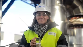 Chercheuse d'IFPEN souriante en casque et gilet de sécurité, tenant un flacon sur un site industriel