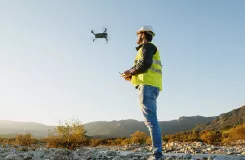 Technicien en casque et gilet de sécurité pilotant un drone sur un terrain rocailleux