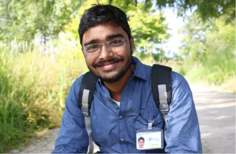 Jeune homme souriant avec badge et sac à dos, dans un parc