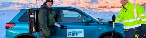 Deux techniciens réalisant des mesures avec un équipement portable à côté d'un véhicule Flair, dans un paysage enneigé