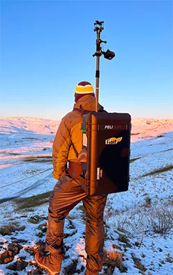 Photo d'un collaborateur IFPEN portant sur le dos une FlairBox pour analyser la qualité de l'air dans un paysage de montagne, en hiver