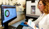 Chercheuse en blouse consultant un document devant un écran affichant des données, dans un laboratoire