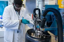 Technicien en blouse et gants manipulant un équipement de laboratoire au-dessus d'un réservoir cryogénique